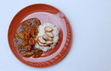 Top view, Yellow Curry Chicken with cooked rice in the round orange color of dish on white floor.