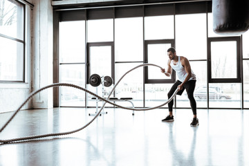 selective focus of strong sportsman exercising with battle ropes in modern gym