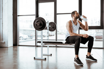 handsome sportsman drinking protein milkshake near barbell in gym - obrazy, fototapety, plakaty