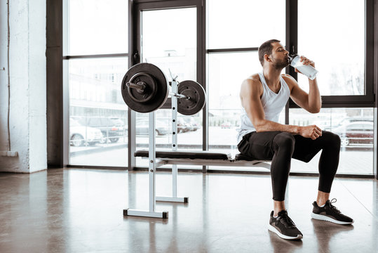 Handsome Sportsman Drinking Protein Milkshake Near Barbell In Gym