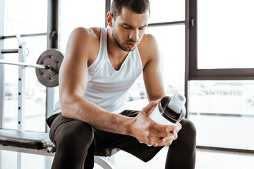 tired sportsman holding sports bottle with protein milkshake in gym