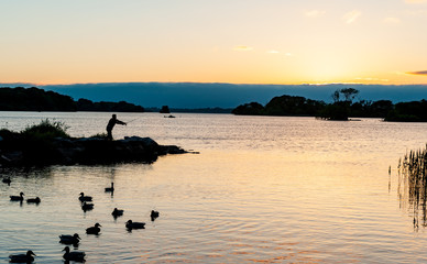 Naklejka premium Silhouette of man casting a fishing rod on the lakes of Killarney national park at sunset