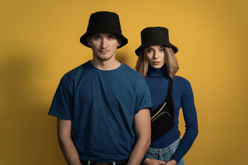 Portrait young pretty man and woman in blue t-shirts and black caps posing on yellow background