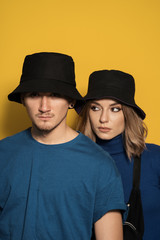 Portrait young pretty man and woman in blue t-shirts and black caps posing on yellow background