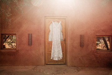 Robe de mariée pendue à une porte typique en bois avec un rayon de soleil pour un mariage bohème