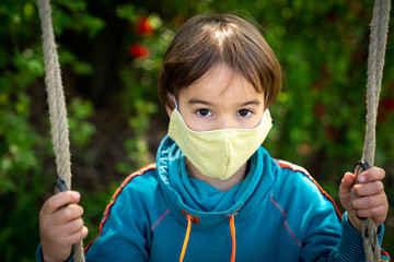 Child with face mask is sitting on a swing