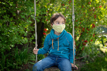 Child with face mask is sitting on a swing