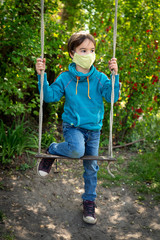 Child with face mask is sitting on a swing