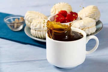 Drop falling into a cup of coffee. On a light blue wooden background. lump sugar fell into a mug with coffee and caused a splash of coffee