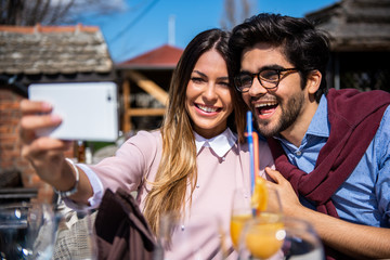 Happy young couple is doing selfie, looking at camera and smiling while sitting at the cafe