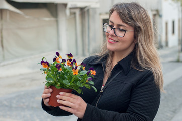 happy blonde woman holding a beautiful vase of colorful flowers on the street.