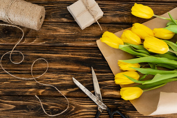 top view of yellow tulips near scissors, jute twine rope and gift box on wooden surface, mothers day concept