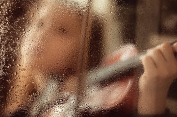 Girl with a violin behind a glass window with drops of water, low key. Music concept