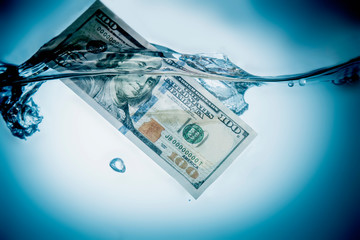 US Dollar banknotes sinking in water as symbol of global financial crisis and uncertain future of international trade and investment. Selective focus. Horizontal image.