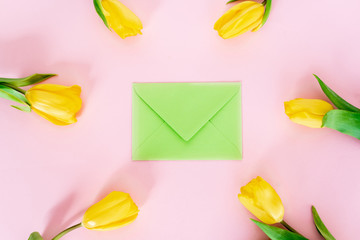 top view of green envelope near yellow tulips on pink, mothers day concept