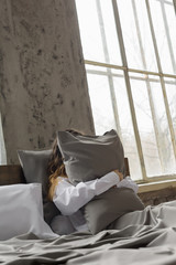 woman hugging pillow, pillow made of silk fabric, quality bedding, large window in the interior