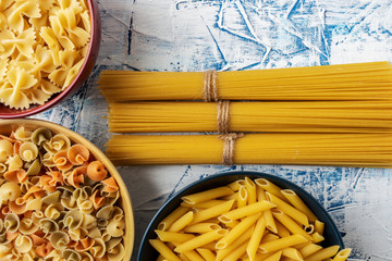 bundles of spaghetti and ceramic bowls with various pastas on a blue and white textured background