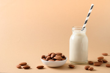 Fresh almond milk in glass bottle and almonds nuts on beige. Close up.