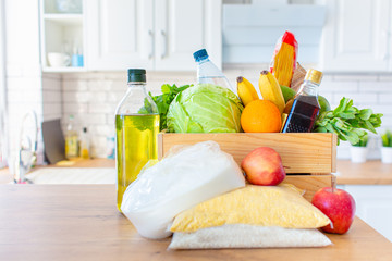 A wooden box of different food, fruit, vegetables, oil, water, sugar on the kitchen. Safe home delivery.