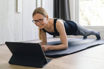 Fototapeta na wymiar Frau macht Planks zu Hause auf der Fitnessmatte mittels Online-Kurs und lächelt dabei