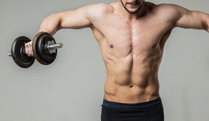 Bodybuilder athlete doing exercise with dumbbell on a light background