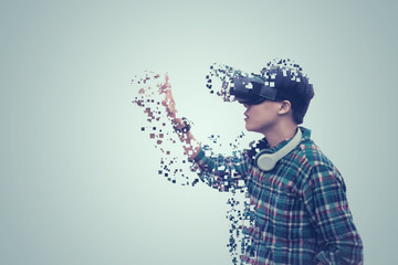  Asian man wearing glasses of virtual reality dissolving into pixels is touching on gray background Future Technology Concept