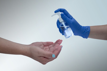 Close up hands of woman applying alcohol gel in hand with grey studio background. 