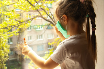 a masked child on a windowsill looks out the window. carontin. self isolation. baby at home.