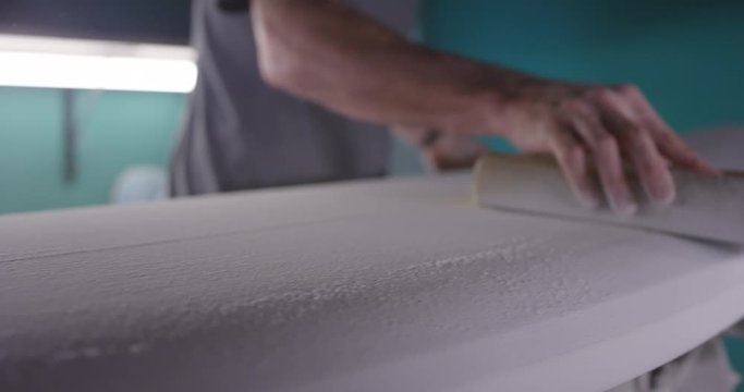 Man sanding surfboard in workshop
