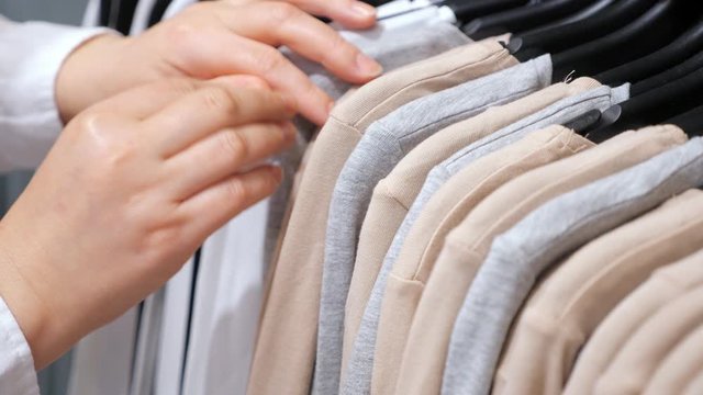 Female hands sort cotton pullovers on a hanger in a clothing store. Close-up.