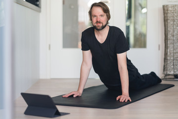 Mann macht Yoga-Übung zu Hause mittels online-kurs auf der Fitnessmatte