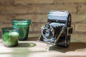 Old vintage camera with two beautiful green candles. Old wall brick in the ground. Wooden ground.