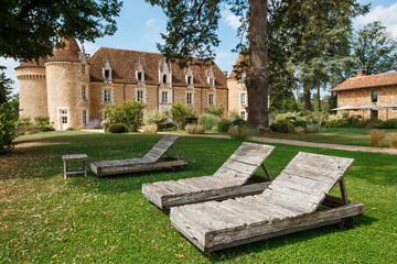 Wooden sunbeds standing on the background of old chateau. Luxury place for the rest and retreatment. Chairs for relax on beautiful garden