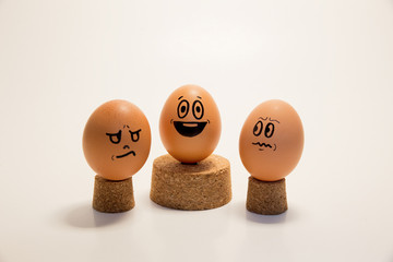 Egg with face standing in the middle of venvious and angry eggs. Cork stopper. White background. Concept of positive thinking.