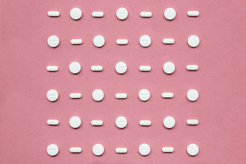 Geometric series of a white tablets on  pink uniform paper background. Idea of people's addiction to drugs.