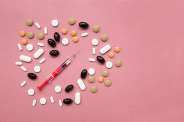 Close up of medical 
syringe with several tablets with different color, shape e dimension as frame. Pink uniform paper background. Idea of addiction to drugs.