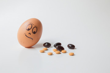Close up of egg with doubtfully and 
disapproving face watching at a group of tablets with different color, shape e dimension. White uniform paper background. Idea of addiction to drugs.