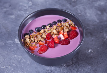 Smoothie bowl with berries and muesli on the gray table.