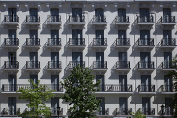 Building with geometric structure of windows and balconies creating an optical illusion with shadows. 
trees in the foreground.