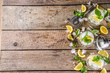 Boozy lemon basil lemonade, with fresh basil leaves, lemons and crushed ice, rustic wooden background copy space