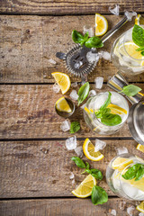 Boozy lemon basil lemonade, with fresh basil leaves, lemons and crushed ice, rustic wooden background copy space
