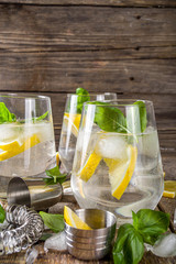 Boozy lemon basil lemonade, with fresh basil leaves, lemons and crushed ice, rustic wooden background copy space