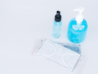 Surgical face masks in a plastic package, an alcohol spray bottle and alcohol gel bottle on white background.