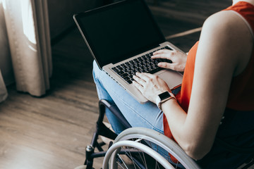 Woman in a wheelchair at home with a laptop on her lap, hand close up, unrecognizable man.
