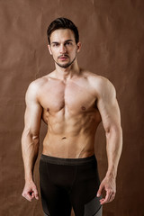 Fototapeta na wymiar Handsome sportsman bodybuilder posing on brown craft background