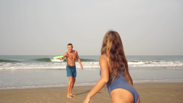 A young couple plays frisbee on the beach. Lovers throw a flying disc at sea
