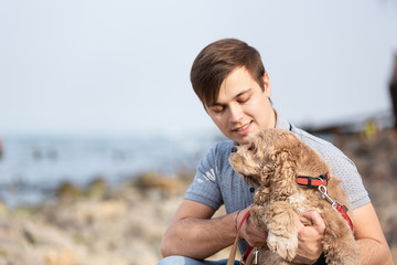 Young man hugging a dog at the sea shore. The man petting obedient dog on a sea coast. Best friends.