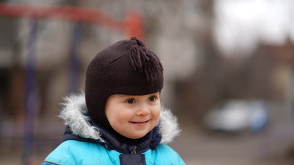 Portrait of little cute boy in blue jacket and brown baby cap in playground