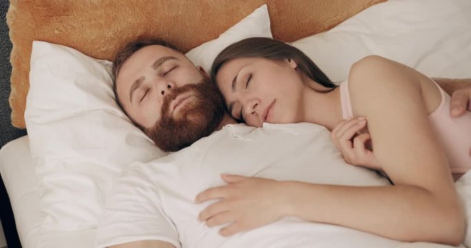 Cute couple cuddling together in bed while sleeping in early morning. Young man and woman lying on bed, dreaming while embracing each other. Zoom in.Concept of relationship.
