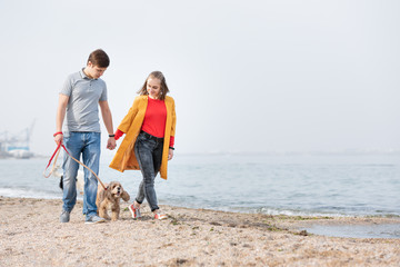 Young couple walking with a dog on a sea coast. Dog walking outdoors.
